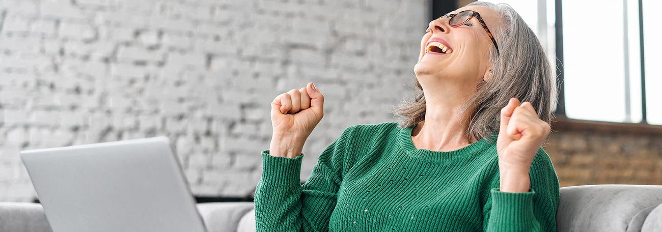 very happy older woman sitting on her sofa with her laptop after getting good news 