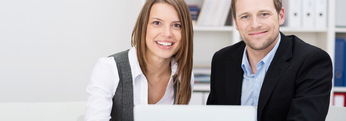 young couple sitting at the table with a laptop smiling as they manage their finances