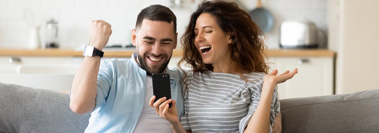 a happy couple relaxing together celebrating a win on her mobile phone game.